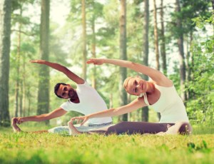 fitness, sport, yoga and people concept - happy couple stretching on mats over green woods background